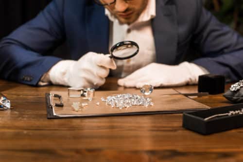 Henkilö tutkii suurennuslasilla pöydällä olevia timantteja